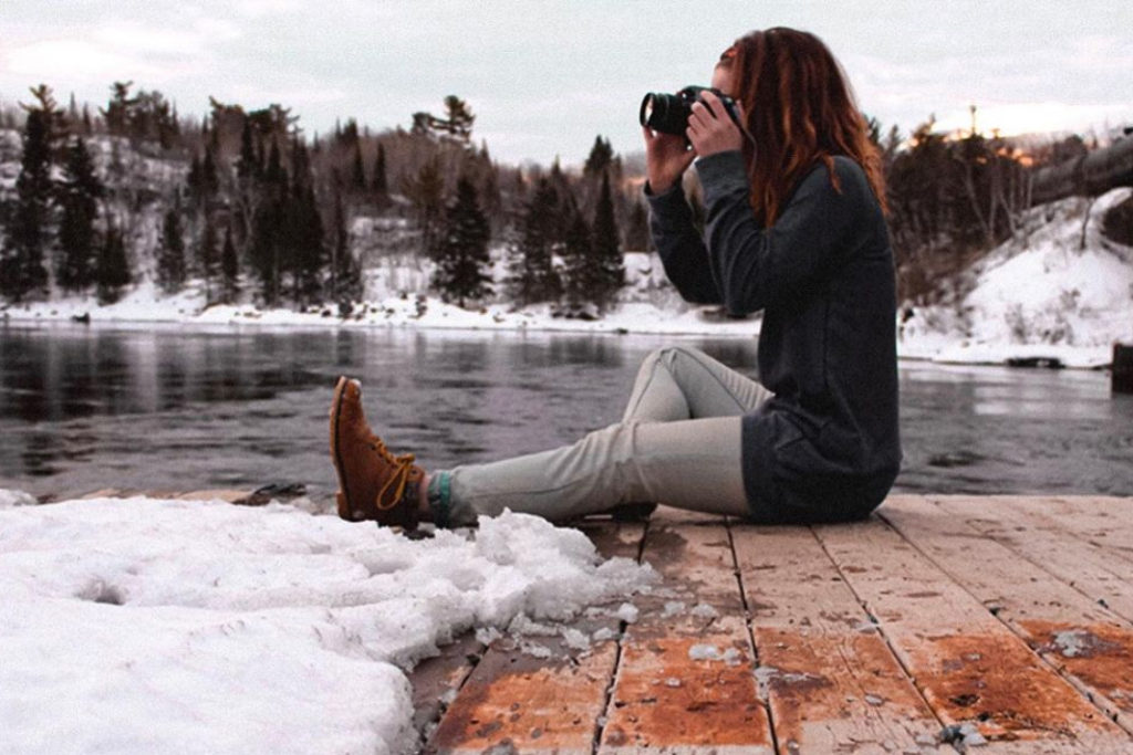 Riley Chervinski sitting on a dock in winter taking a photo.