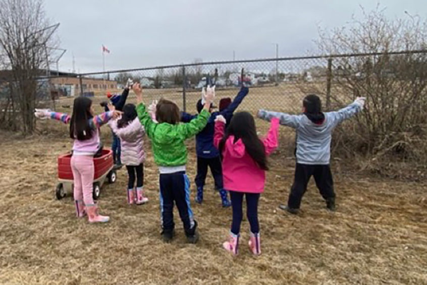 Students face away from the camera with their arms up outside after picking up litter.