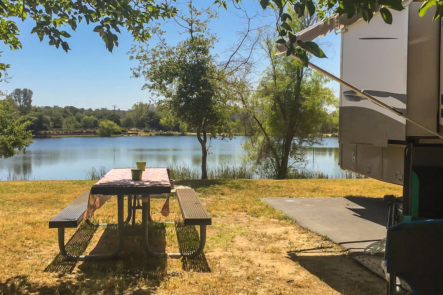 Picnic table beside RV camper and lake.