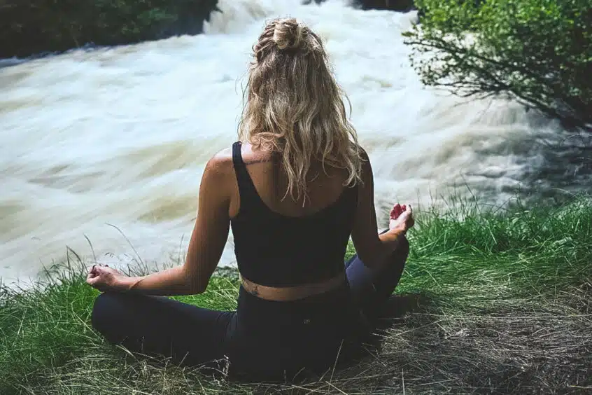 Woman sitting cross-legged in front of rushing water.