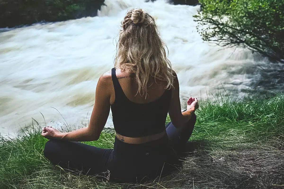 Woman sitting cross-legged in front of rushing water.