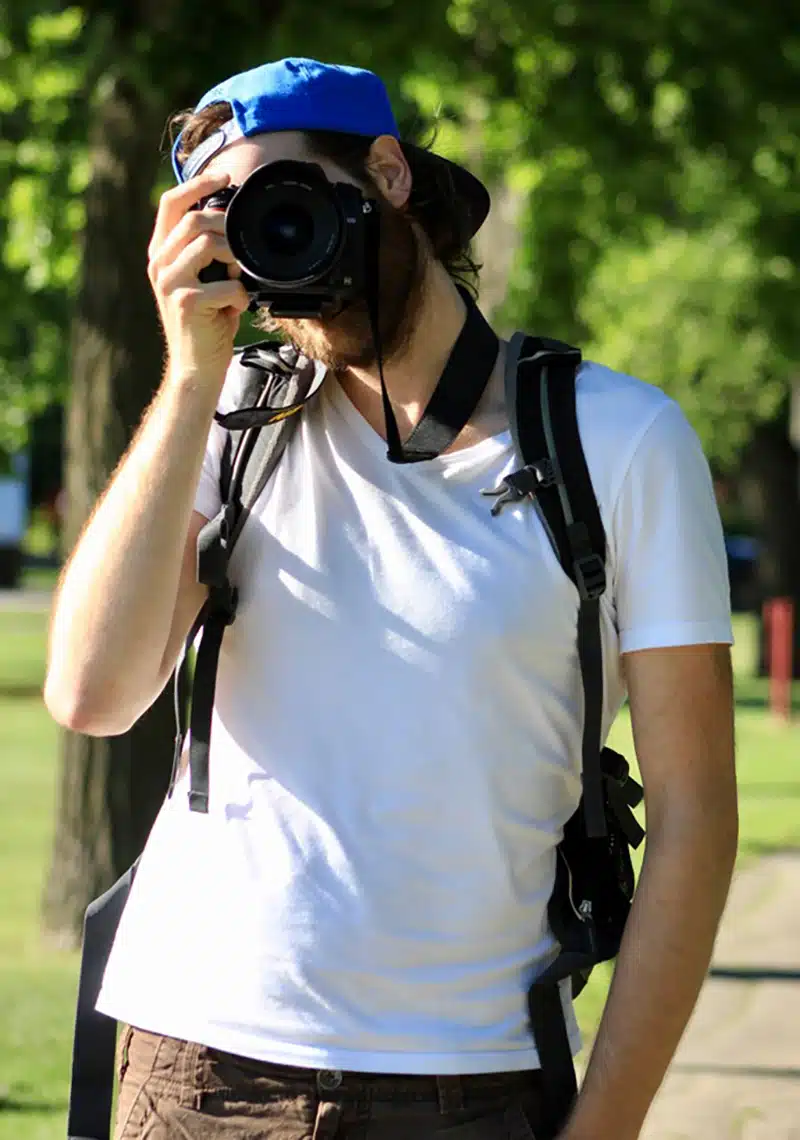 Photographer Kevin Kash in a park holding a camera in front of his face.