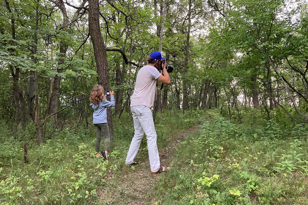 Two people standing in a forest taking photos.