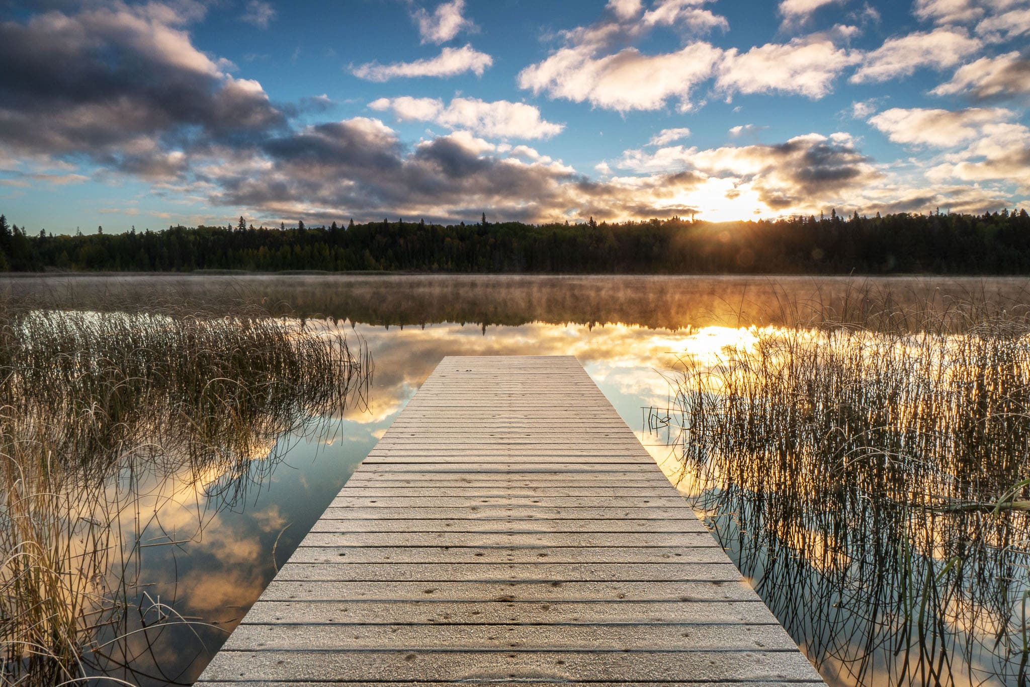 A dock on water in Riding Mountain National Park in fall at sunrise.