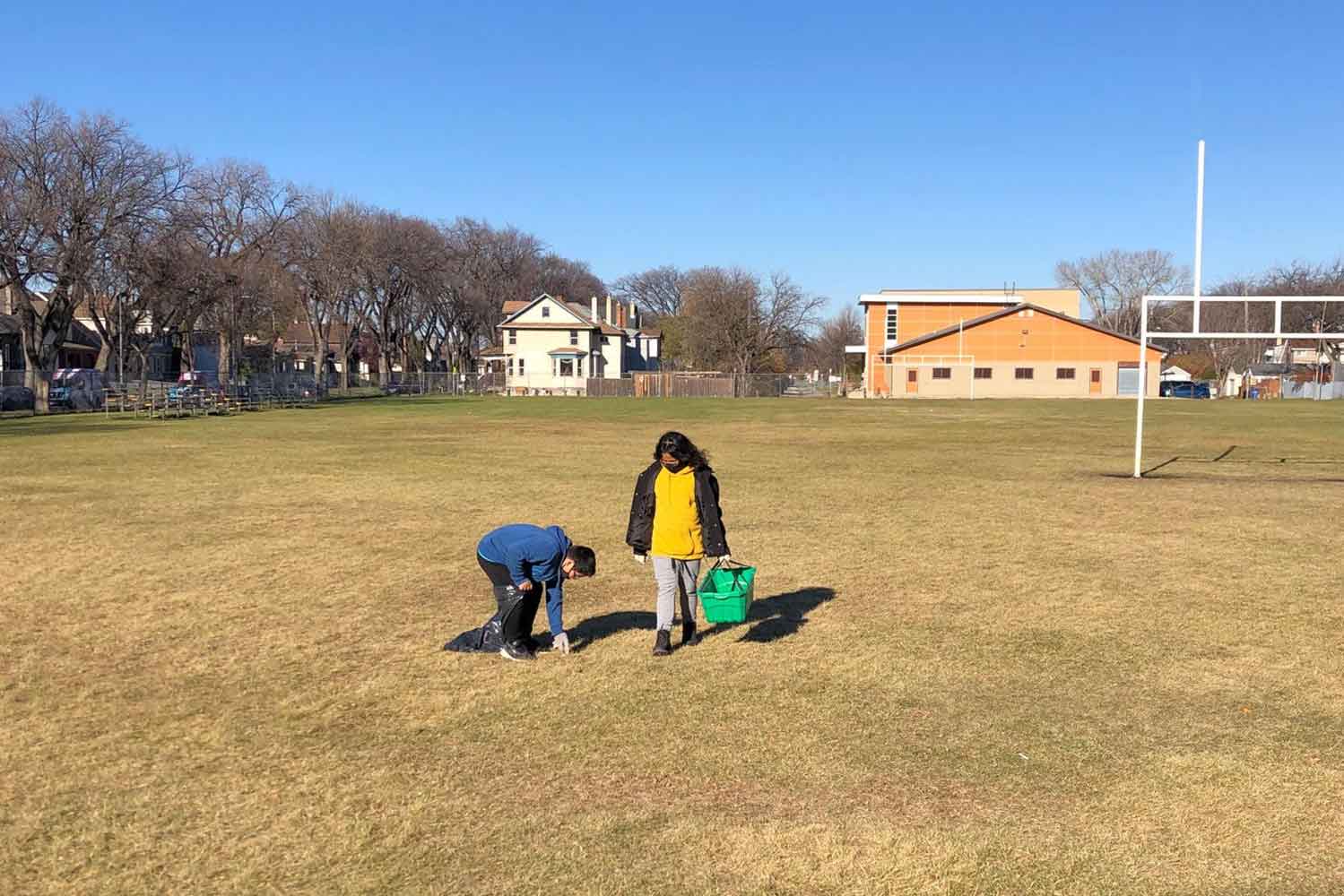Two students pick up litter in a field for the CPAWS Manitoba Student Litter Cleanup Challenge.