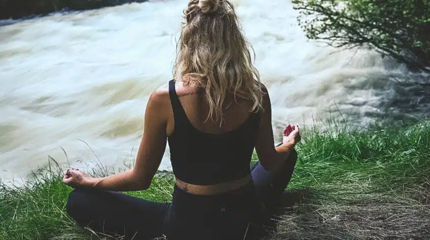 Woman sitting cross-legged in front of rushing water.