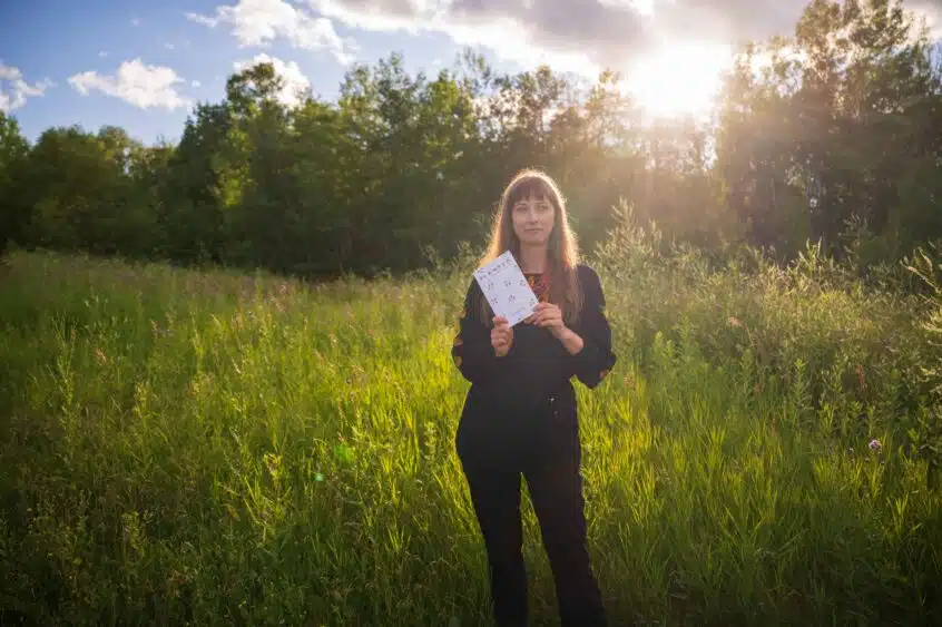 Author Kaitlin Vitt stands in a field holding a copy of her book Planted: Stories From Manitoba’s Natural World.