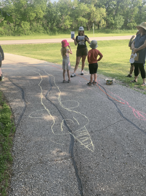 Children standing on bike path in Assiniboine Park. Surrounded by their drawings of whales.