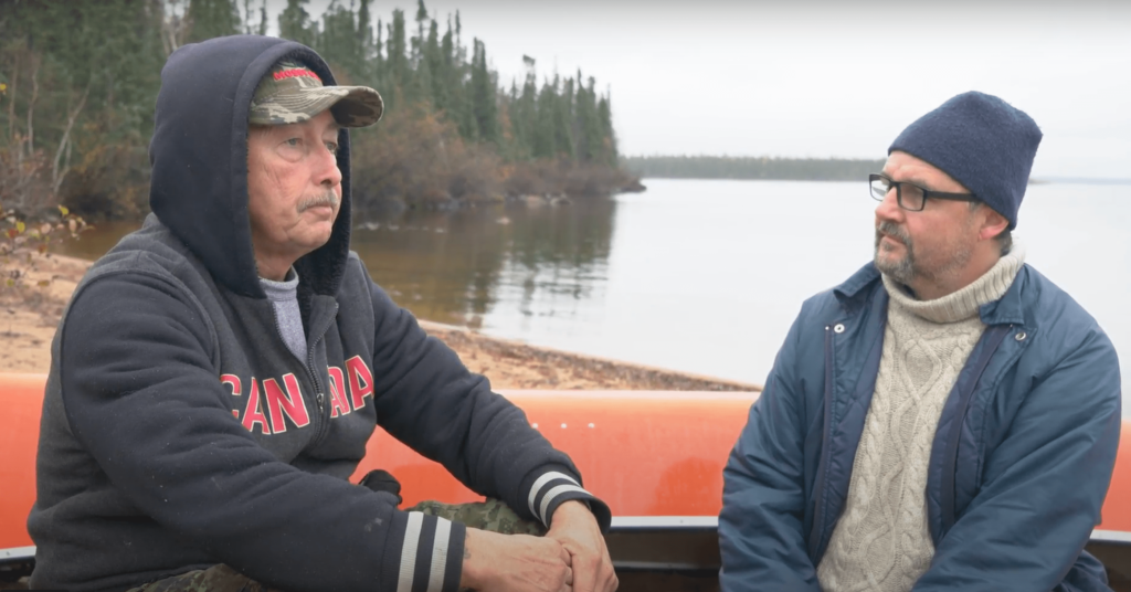 Ernie Bussidor (L) and Ron Thiessen talk on the shore of Tadoule Lake in 2019. Credit Christopher Paetkau