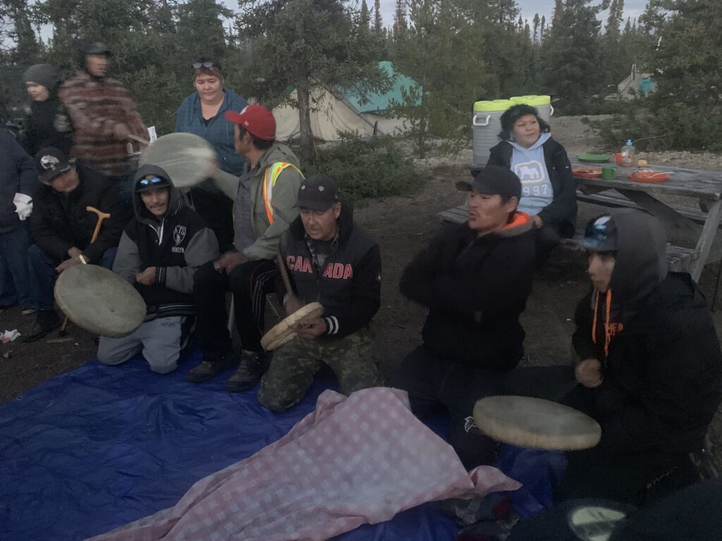 Ernie Bussidor (C, Canada hoodie) and Sayisi Dene First Nation community members play traditional Dene hand games during the 2019 Stewardship Summit. Credit Mira Oberman